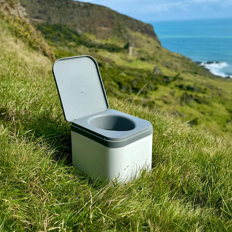 Portable toilet in a grassy outdoor setting with a scenic background